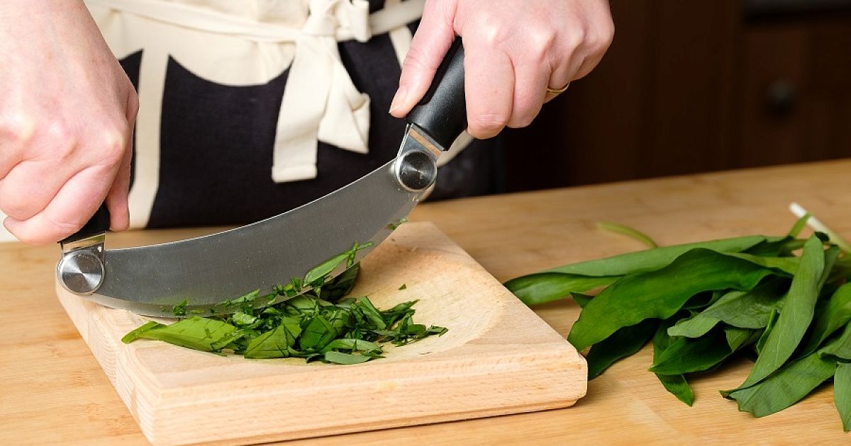 Cutting green. Шеф-повар режет овощи вдалеке на столе. Потом взяла доску и нож и начала нарезать зелень.